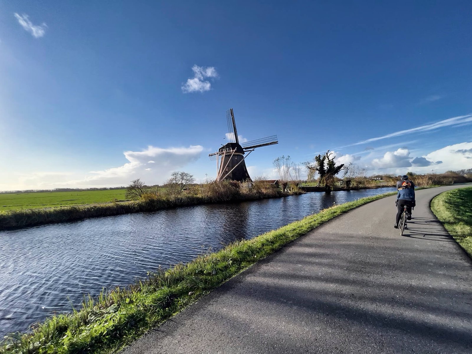 Windmill beside a canal, with a cyclist on the path along the water